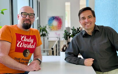 Ronny Büchner und Tino Favetto sitzen nebeneinander und lächeln in die Kamera.