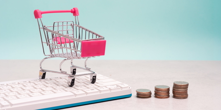 Mini-Einkaufswagen auf Tastatur neben gestapelten Münzen als Symbol für E-Commerce-Kosten