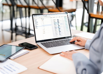 Person working on a laptop with a Perfion interface at a desk, with tablet, smartphone and notebook nearby