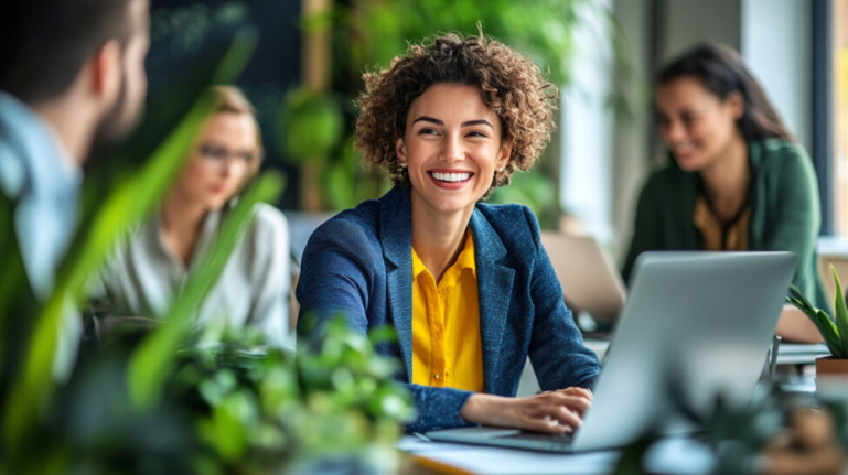 Smiling woman in yellow blouse working on laptop in green office setting