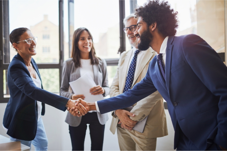 Two people shake hands and two others stand next to each other