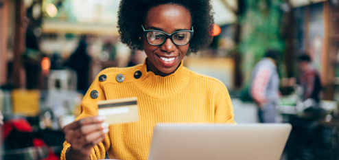 Woman in a yellow sweater using a laptop and holding a credit card