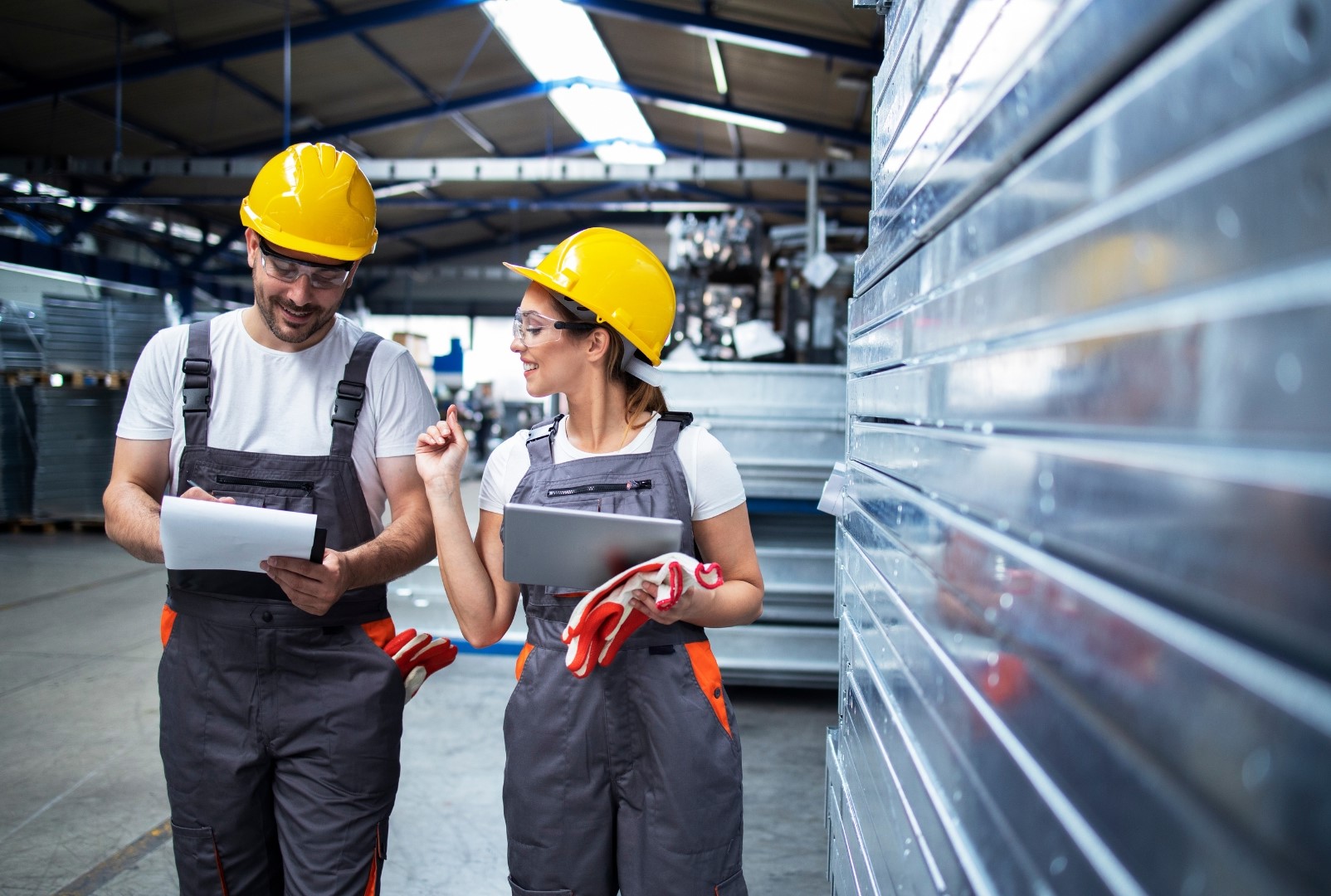 Two people with safety clothing and notepad in a warehouse